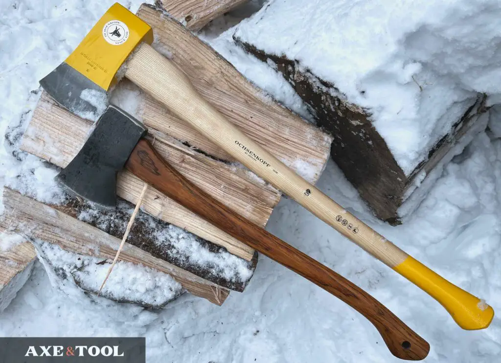 a curved handled boys axe and straight handled splitting axe sitting on a log in the snow