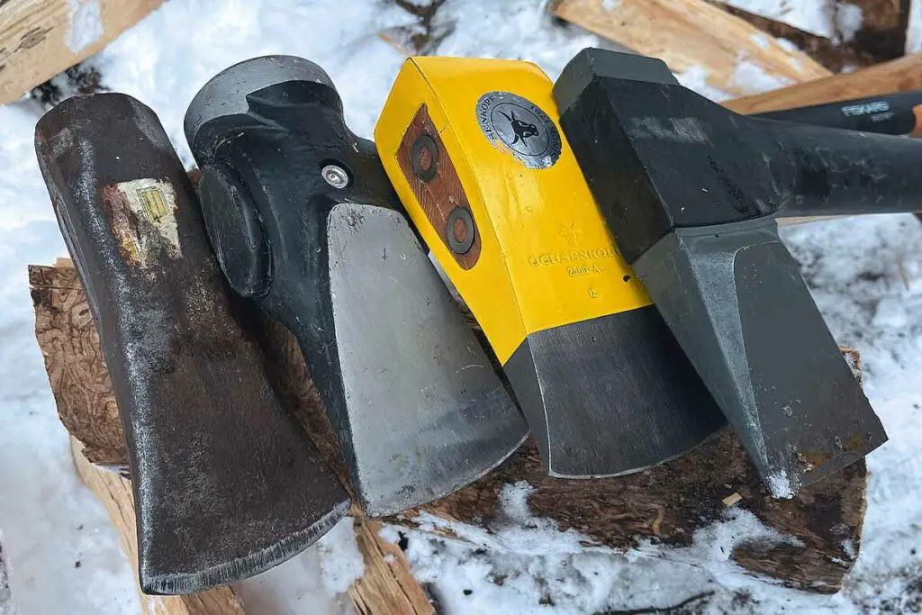 An assortment of mauls and splitting axes leaning on a log in the snow