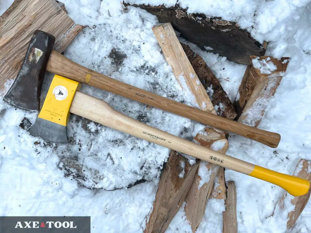 Wood handled splitting axe and maul sitting on a log in the snow